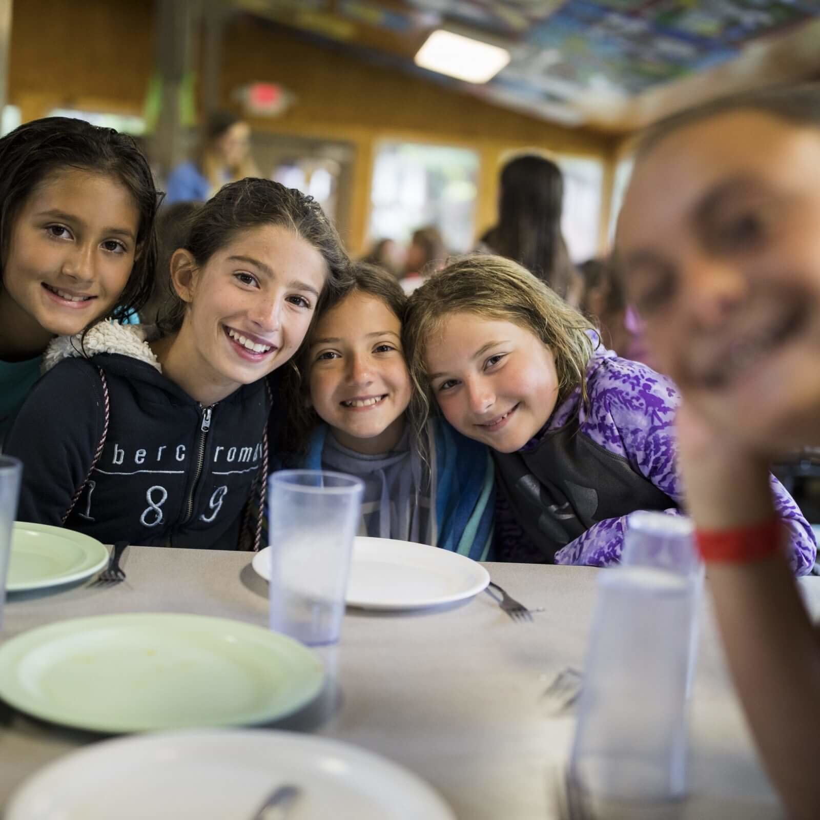 A group of kids sitting at a dining hall table smiling.