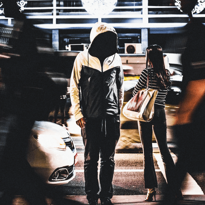 A person standing in a rushing crowd with a hood over their face