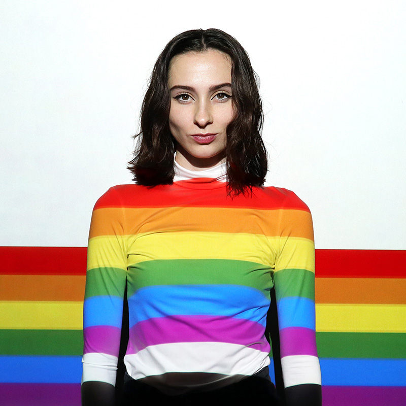 LGBTQIA+ person in front of rainbow wall LGBTQIA+ person in front of rainbow wall