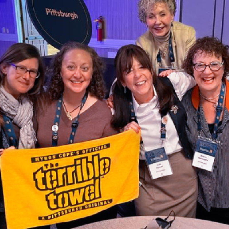 A photo of a group of women holding a yellow towel that says 